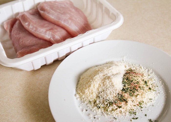a tray of raw turkey Cutlets with a garlic and Parmesan mix on a white plate