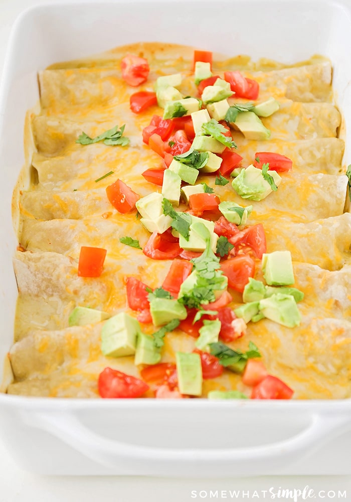 casserole pan filled with green enchiladas and topped with fresh tomatoes and cilantro